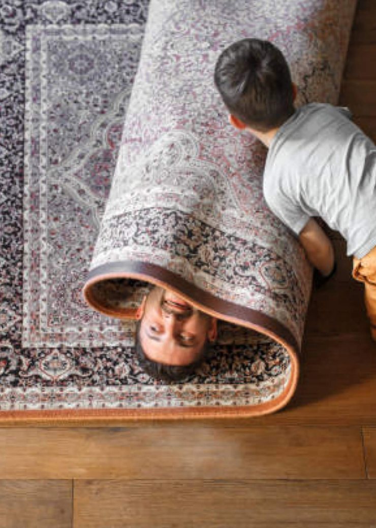 child rolling father up in a carpet playing on hardwood floors